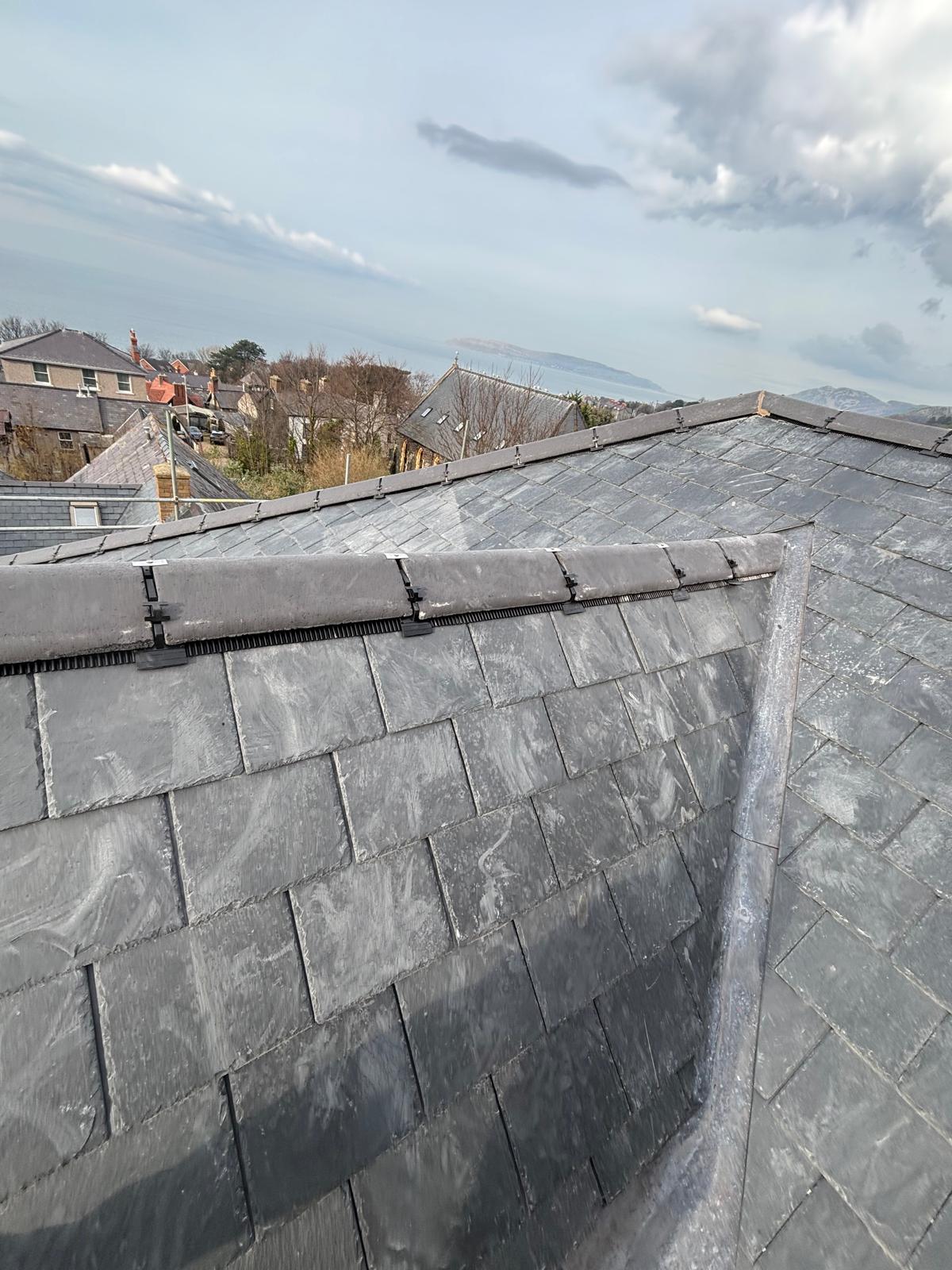Completed natural slate roof with lead valleys against a clear sky